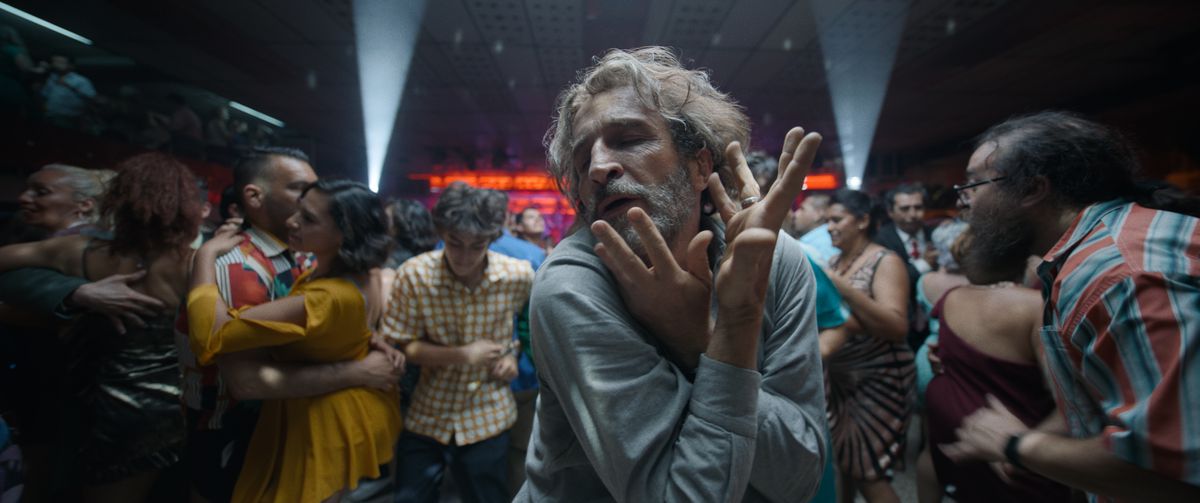 A bearded man (Daniel Giménez Cacho) dancing in a crowded dancehall flanked by shafts of light.