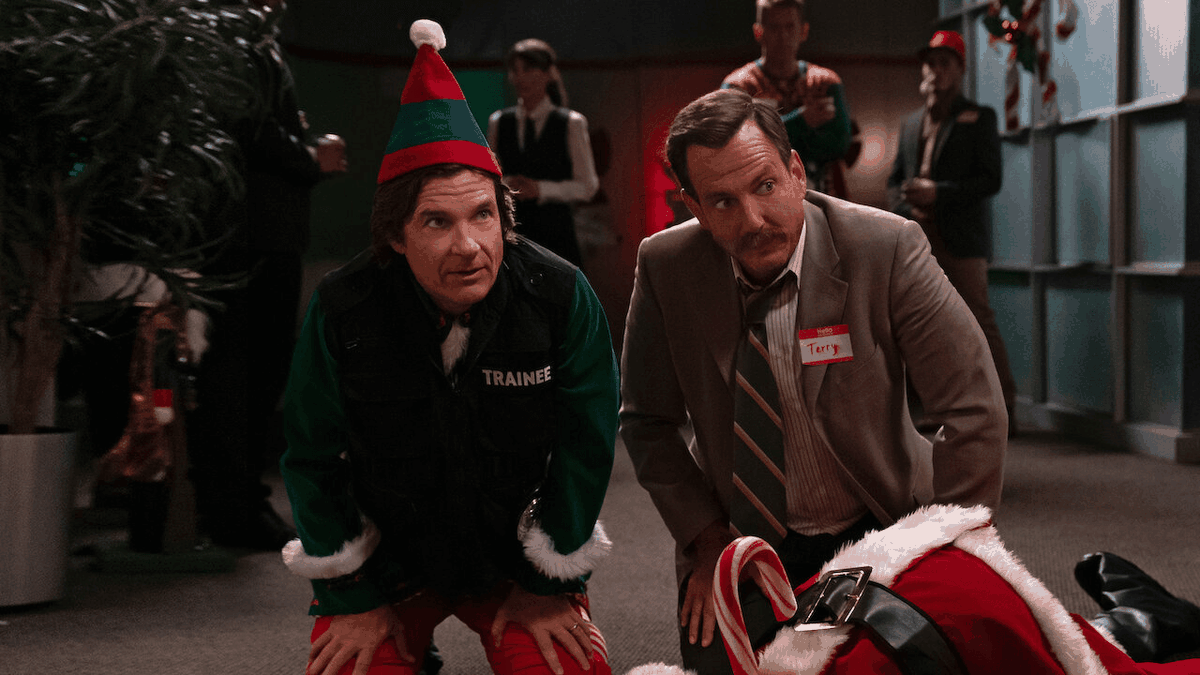 A police detective (Will Arnett) wearing a nametag that reads “Terry” kneels next to a man in a elf costume (Jason Bateman) beside the corpse of Santa Claus.