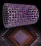 Un'illustrazione della struttura del magnete quantistico simulato dal processore quantistico D-Wave e dal processore che lo ha simulato. Il magnete quantistico si presenta come un reticolo di palline colorate (che rappresentano gli atomi) disposte in un tubo cavo. Il processore sembra un chip di computer.