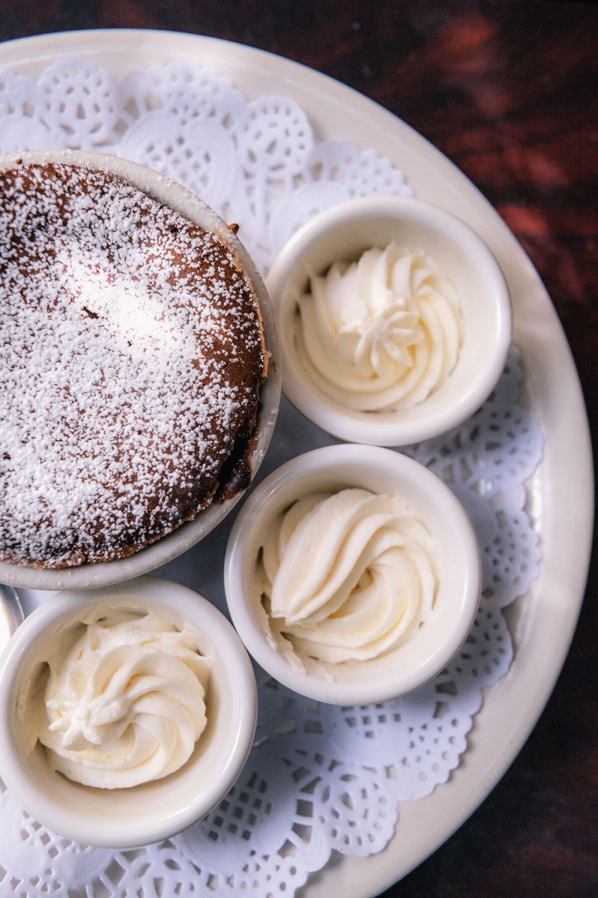 A plate holds a souffle and small cups of whipped cream.