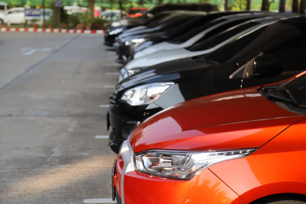 Cận cảnh mặt trước của chiếc ô tô màu đỏ với những chiếc ô tô khác đang đỗ trong khu vực đỗ xe.