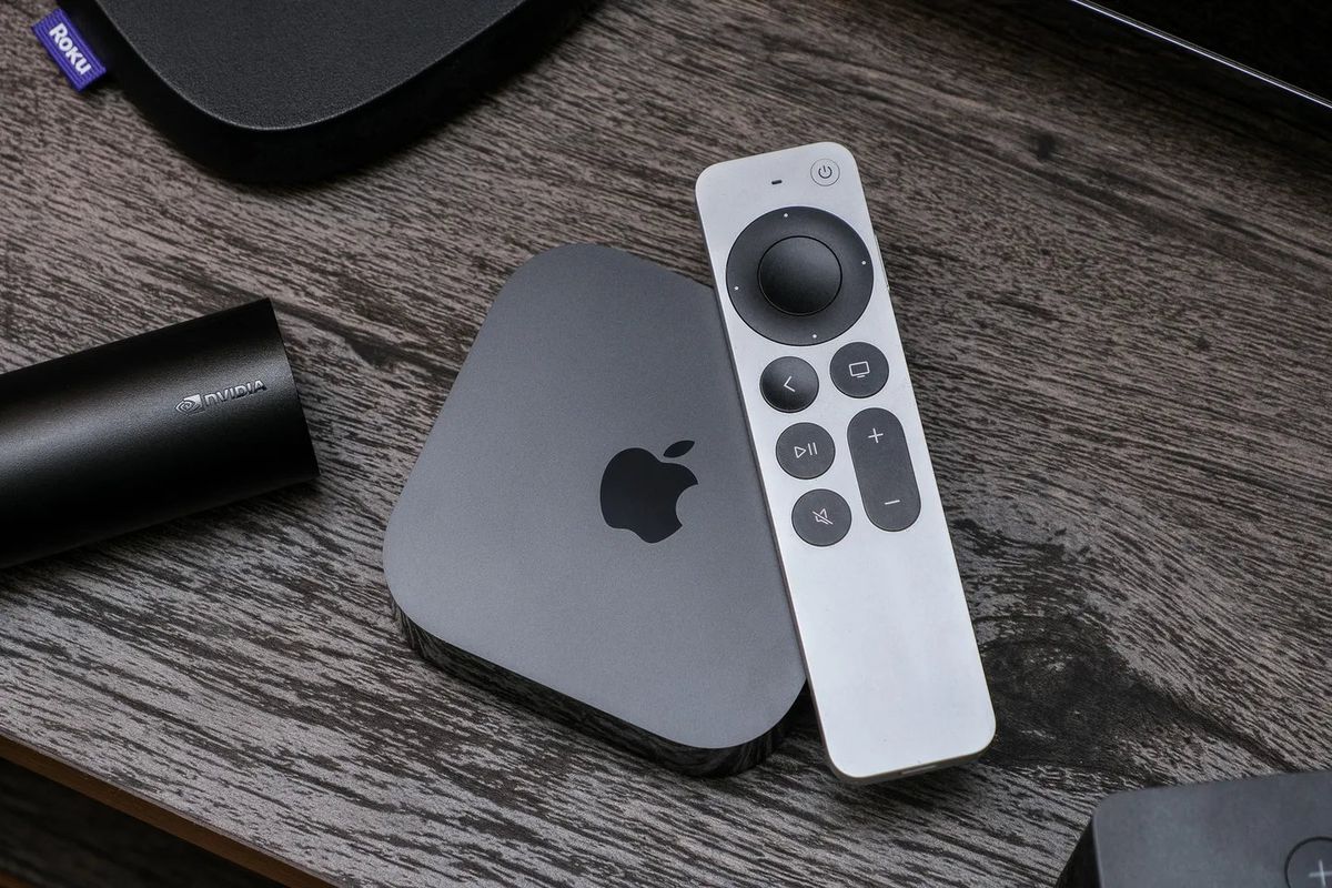 The Apple TV 4K sitting on a wooden entertainment center. The Siri Remote is on top of it.
