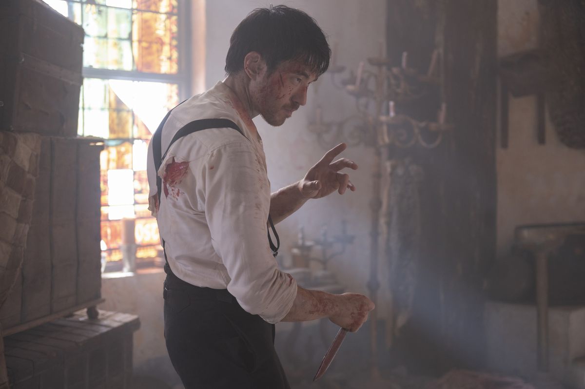 Andrew Koji, with blood on his white shirt and face, holds a knife in a fighting stance in Warrior.