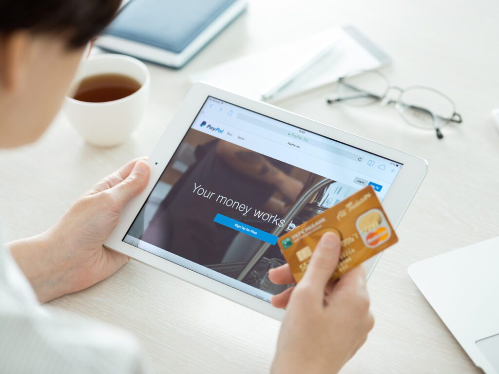 Kiev, Ukraina - 27 Juni 2014: Orang dengan kartu kredit di tangan melihat Apple iPad Air baru dengan situs Paypal di layar. Paypal adalah layanan bisnis e-commerce di seluruh dunia yang memungkinkan pembayaran dan transfer uang melalui internet, didirikan pada bulan Juni 1998.