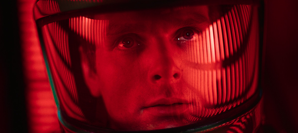 A man in a space helmet stares up at rows of red illuminated columns of light.