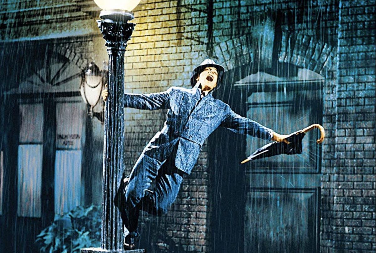 Gene Kelly dancing in a raincoat with an umbrella in Singin’ in the Rain.