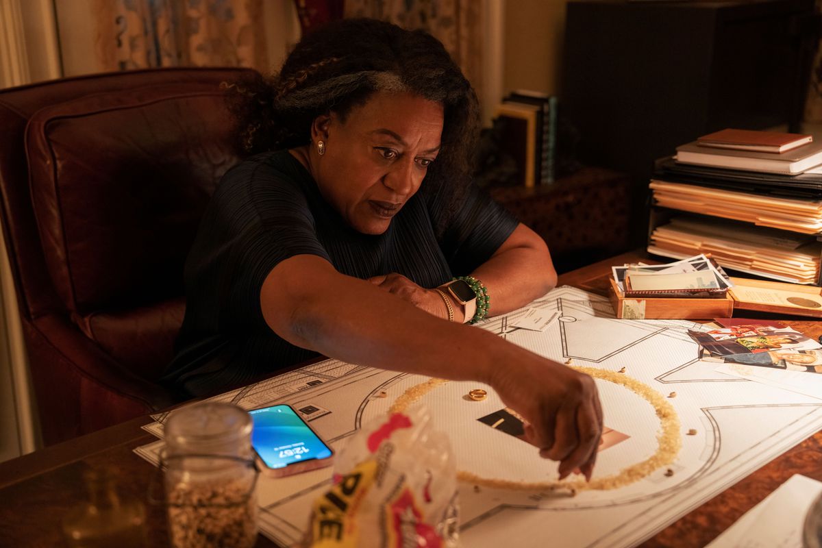 CCH pounder playing a crime boss sitting at her old wooden desk preparing a circular ritual using yellow crystals