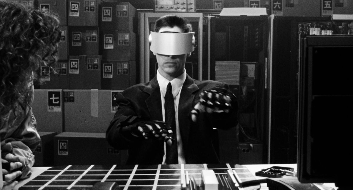 Keanu Reeves as Johnny Mnemonic wearing a VR headset and gloves reaching his hands forward in Johnny Mnemonic: In Black and White.