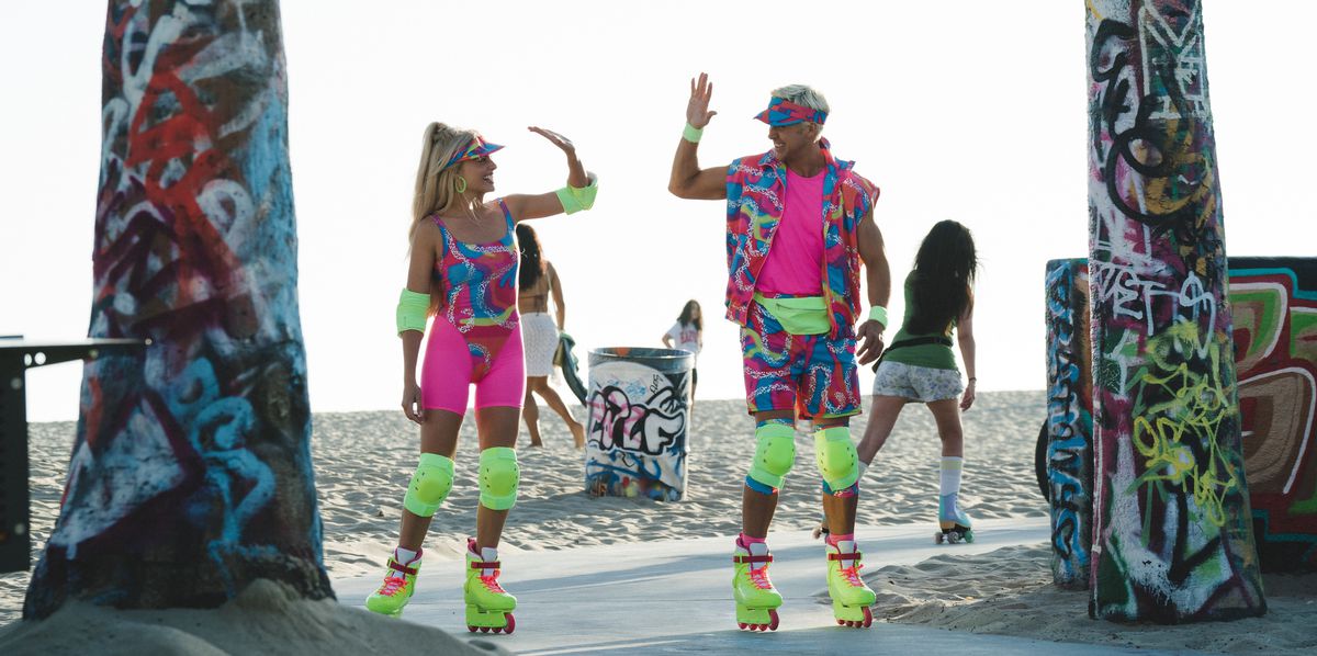 Barbie (Margot Robbie) and Ken (Ryan Gosling), both wearing garish, patterned neon skating outfits and incredibly bright neon-yellow kneepads and Rollerblades, stand in front of a beach between two trees covered in graffiti and go in for a high-five in the 2023 live-action movie Barbie