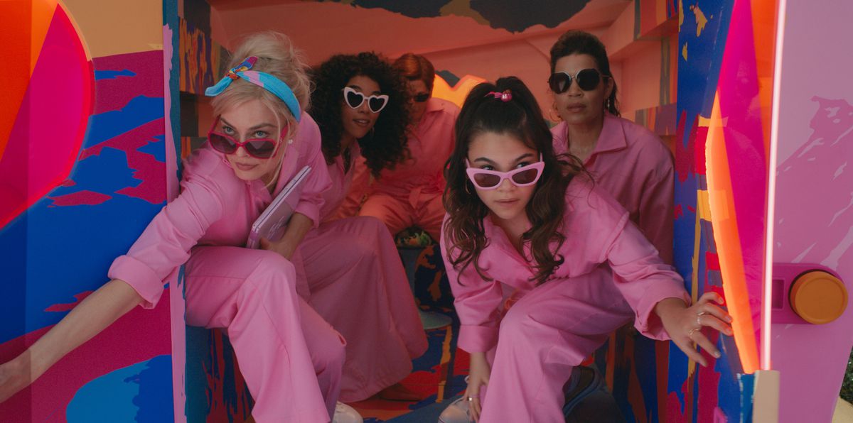 The back of a garishly neon-painted panel van opens to reveal five people in matching powder-pink jumpsuits and nonmatching pink-rimmed sunglasses: Barbie (Margot Robbie), also Barbie (Alexandra Shipp), Allan (Michael Cera), Sasha (Ariana Greenblatt), and Gloria (America Ferrera), in the live-action 2023 movie Barbie