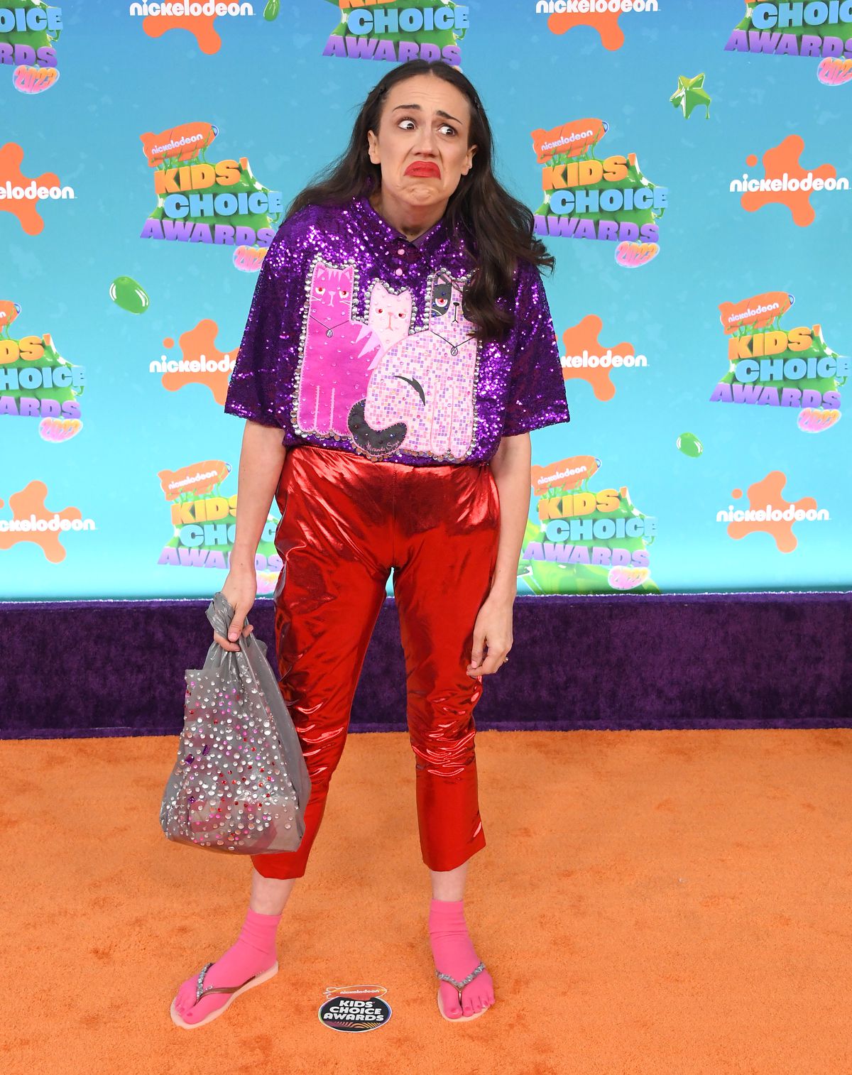 Colleen Ballinger dressed in character as Miranda Sings at the 2023 Kids’ Choice Awards. She’s wearing a sequined cat top, shiny red pants pulled up, and pink socks with flip-flops.