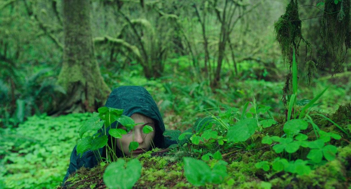 Thomasin McKenzie peers behind some very green petals in the middle of the forest in Leave No Trace.