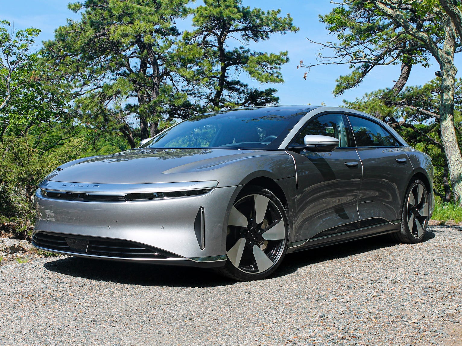 A silver Lucid Air Grand Touring Performance electric car in a driveway, with trees and blue sky in the background.