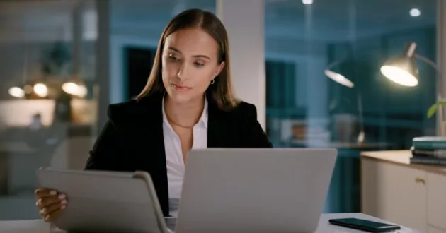 Laptop, focus and tablet with business woman at night for planning, networking and email. Data review, governance, technology and professional with female employee and research in office for commitment and proposal