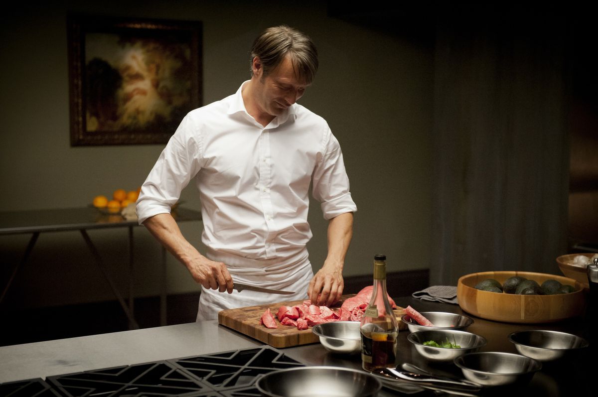 Hannibal (Mads Mikkelsen) chops some meat of dubious origin in Hannibal