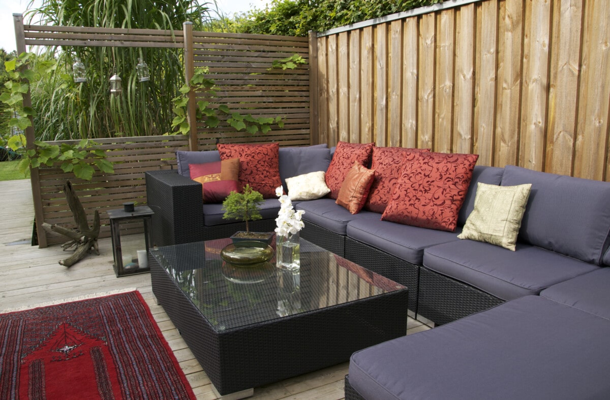 A patio with an outdoor wicker sofa. and private fence