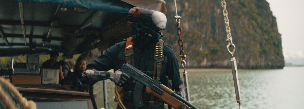 A robot standing in a boat holding an AK-47 with a bandolier of bullets strapped to its chest in The Creator.