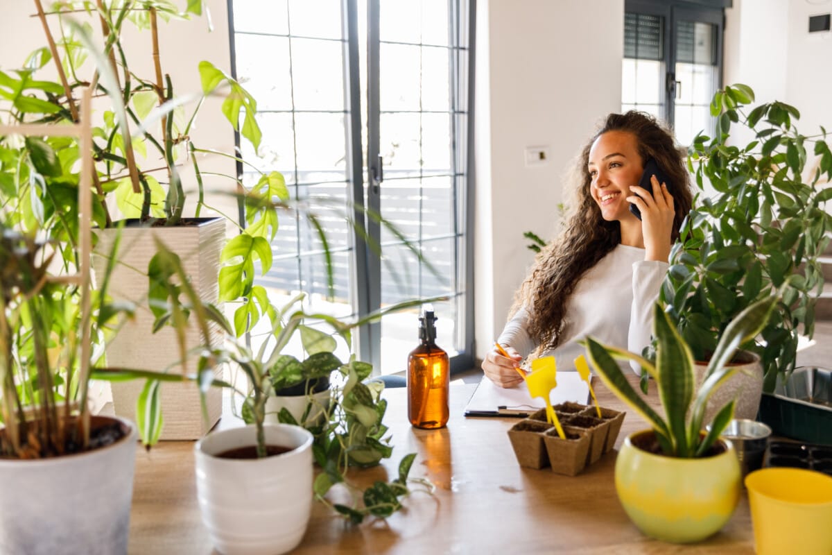 Femeie la telefon înconjurată de plante de casă