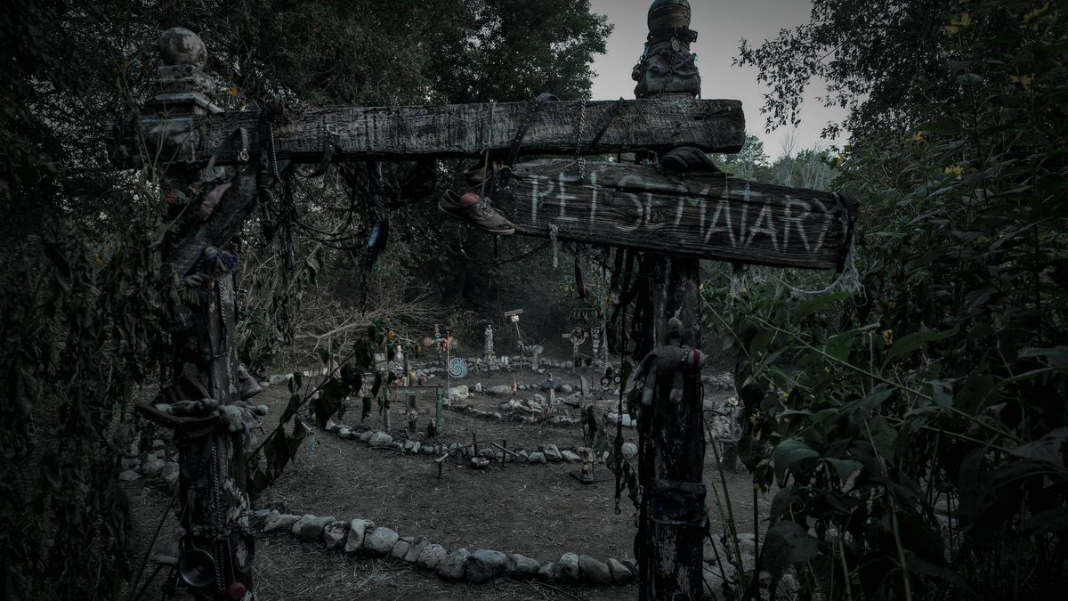 A creepy burial ground in the woods, with grey stones set in a spiral pattern on the ground, framed by a dilapidated wooden gateway with a plank reading “PET SEMATARY,” in Pet Sematary: Bloodlines