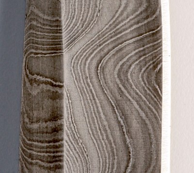 A section of a knife blade with various silver grey and black layered patterns in the metal.