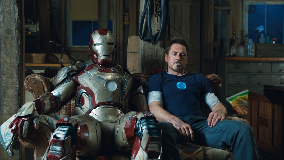 Robert Downey Jr. lounges on a couch next to an Iron Man suit in Iron Man 3.