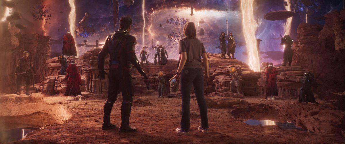 (L-R): Paul Rudd as Scott Lang/Ant-Man and Kathryn Newton as Cassandra “Cassie” Lang in Ant-Man and the Wasp: Quantumania. They stand stock still in an an alien landscape, surrounded by the place’s strange denizens.