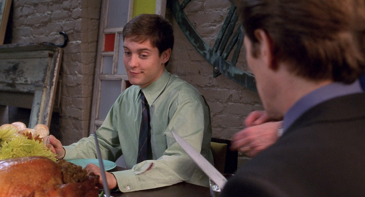 Peter Parker (Tobey Maguire) sourit à Norman Osborn (Willem Dafoe) alors que Norman commence à découper la dinde lors du dîner de Thanksgiving dans Spider-Man 2002 de Sam Raimi.