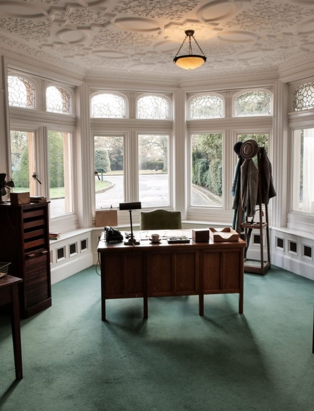 ブレッチリー・パークにあるアラステア・デニストンのオフィスの写真。昔ながらの木製の机、椅子、ランプ、コートラックが置かれている