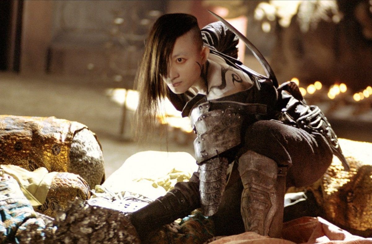 A bad-ass looking villain in Seven Swords, with tattoos and a shaved side of her head, crouches down wearing armor.