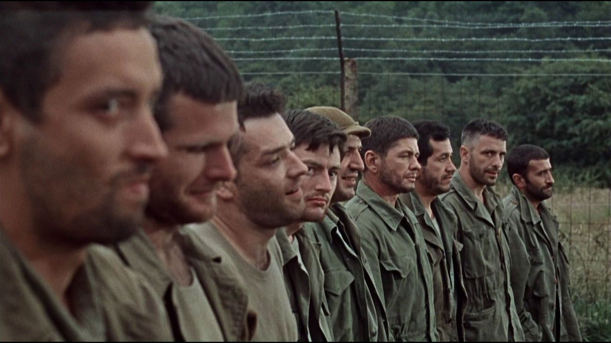 A close-up shot of several soldiers standing in line next to a barbed wire fence in The Dirty Dozen.