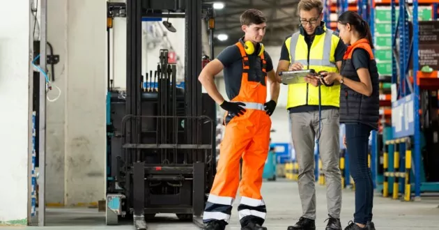 Tiga insinyur berbicara satu sama lain di pabrik sambil melihat iPad