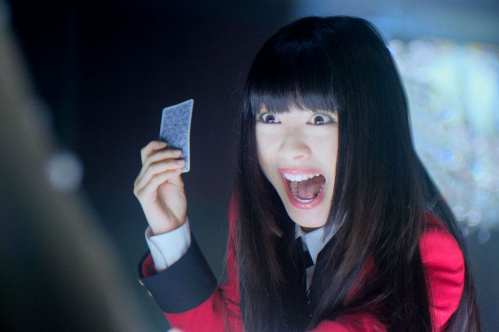 Minami Hamabe as Yumeko Jabami holding up a card and smiling maniacally in Kakegurui.