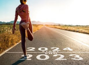 A runner stretches at a starting line that reads "2023 end" and "2024 start"
