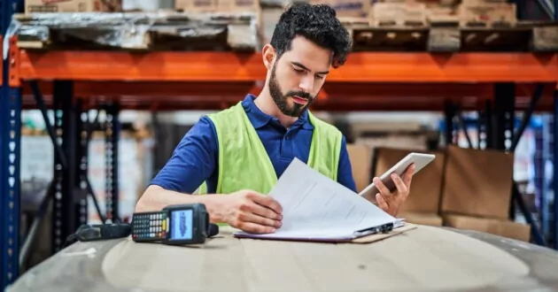 Muncitor de producție se uită prin clipboard și listă de verificare în timp ce ține telefonul în mână