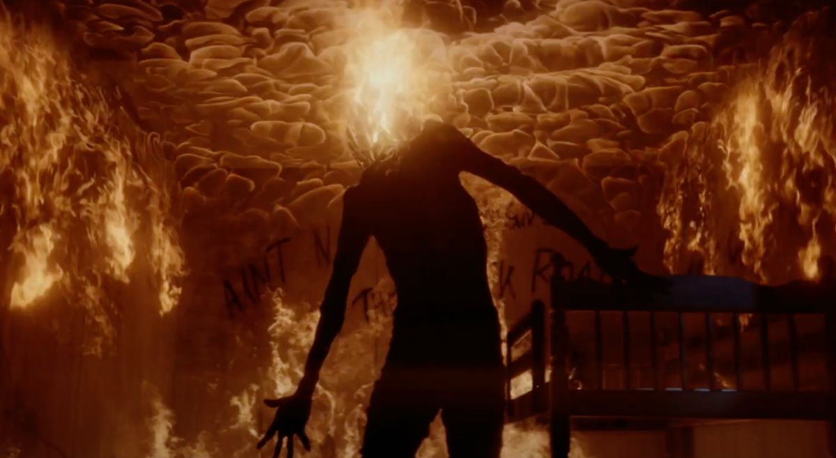 Μια ακέφαλη φιγούρα στέκεται σε ένα δωμάτιο τυλιγμένο στις φλόγες, με ένα λοφίο φωτιάς να εκτοξεύεται από το λαιμό τους στο Dark Harvest.