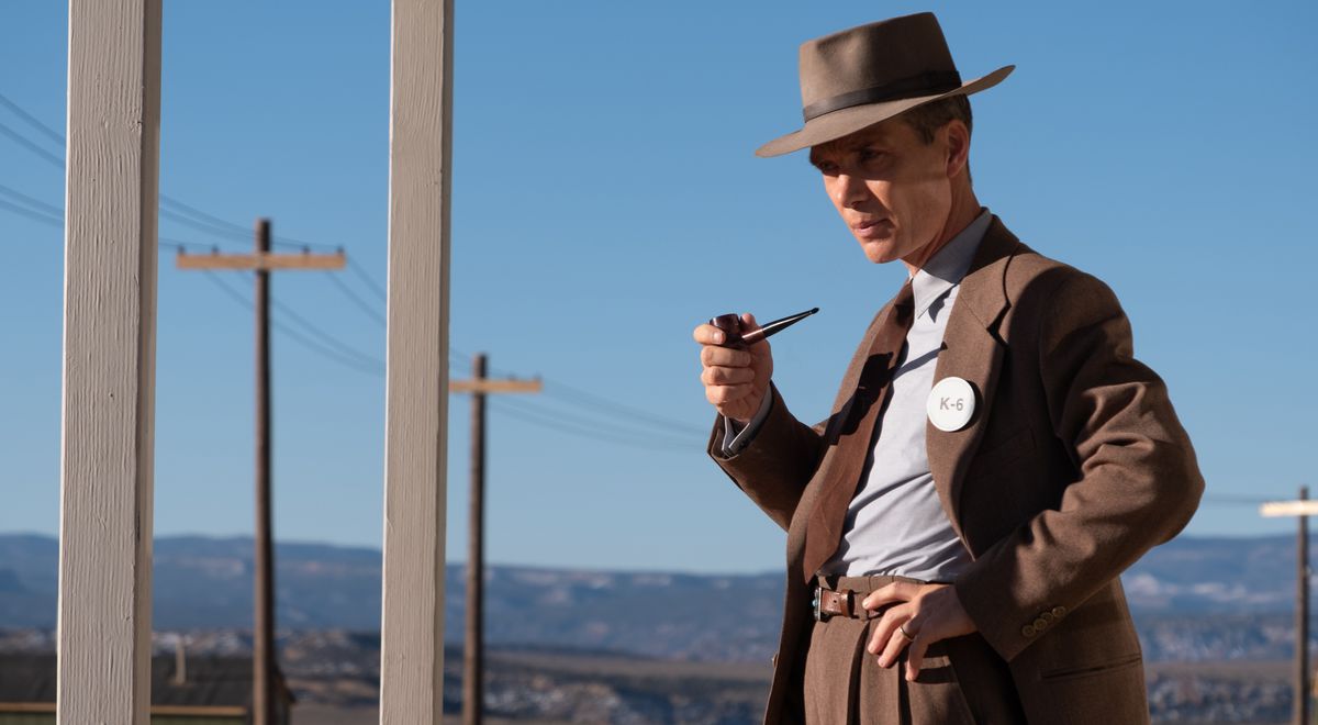 Ο J. Robert Oppenheimer (Cillian Murphy), με καφέ κοστούμι και καπέλο, κρατά έναν σωλήνα και στέκεται σε μια έρημο κοντά σε μια σειρά τηλεφωνικών στύλων στο Oppenheimer του Christopher Nolan