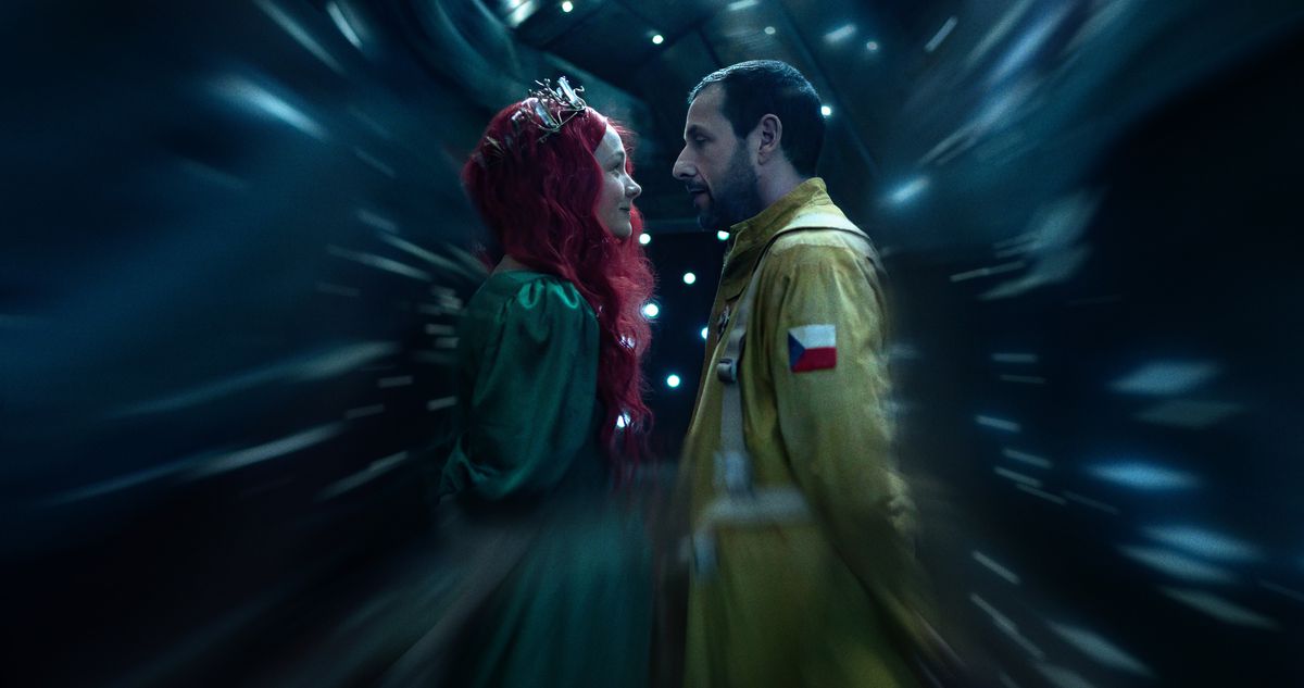 Lenka (Carey Mulligan, in a silver tiara, flowing red wig, and green ballgown) stands close to Jakub (Adam Sandler), dressed as an astronaut in a yellow flight suit, as everything around them blurs in a scene from Netflix’s Spaceman