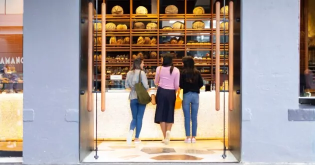 Wide shot through symmetrical doors of young women browsing the delicious food options at an artisanal bakery. Example of a point in the customer experience.