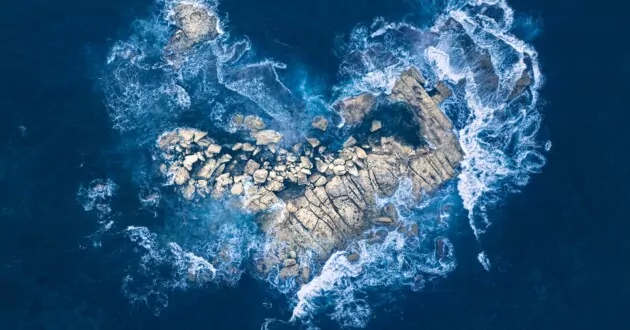 aerial view of rocks in form of heart in ocean, waves crashing against