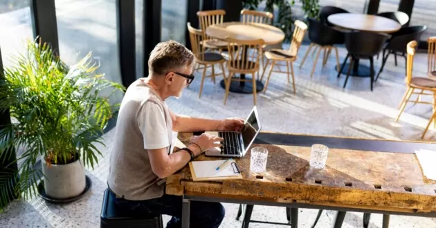 Persoon aan de laptop in een café dat alleen aan tafel zit