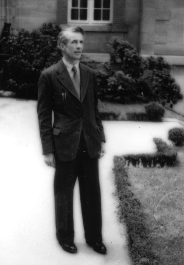 Black and white photograph of a man in a suit outside a large house