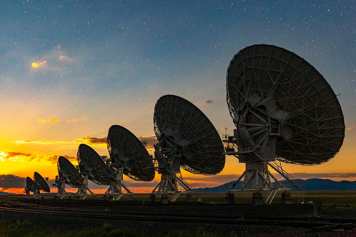 Row of large radio telescopes at sunset
