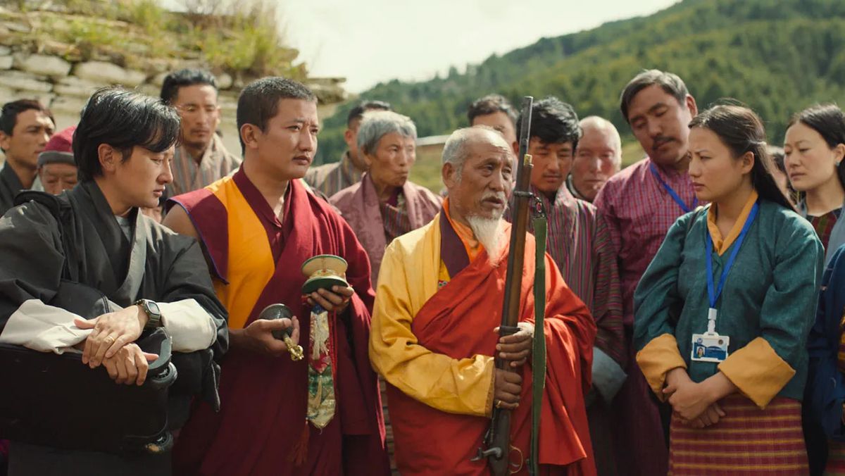 A group of villagers and monks admiring an antique rifle.