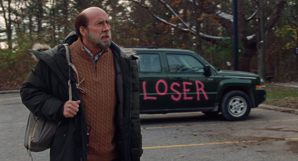 Um Nicolas Cage de aparência desleixada segura uma mochila e fica na frente de um carro com “LOSER” pintado em letras rosa brilhante em Dream Scenario.