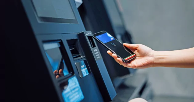 Рука человека с помощью телефона в банкомате