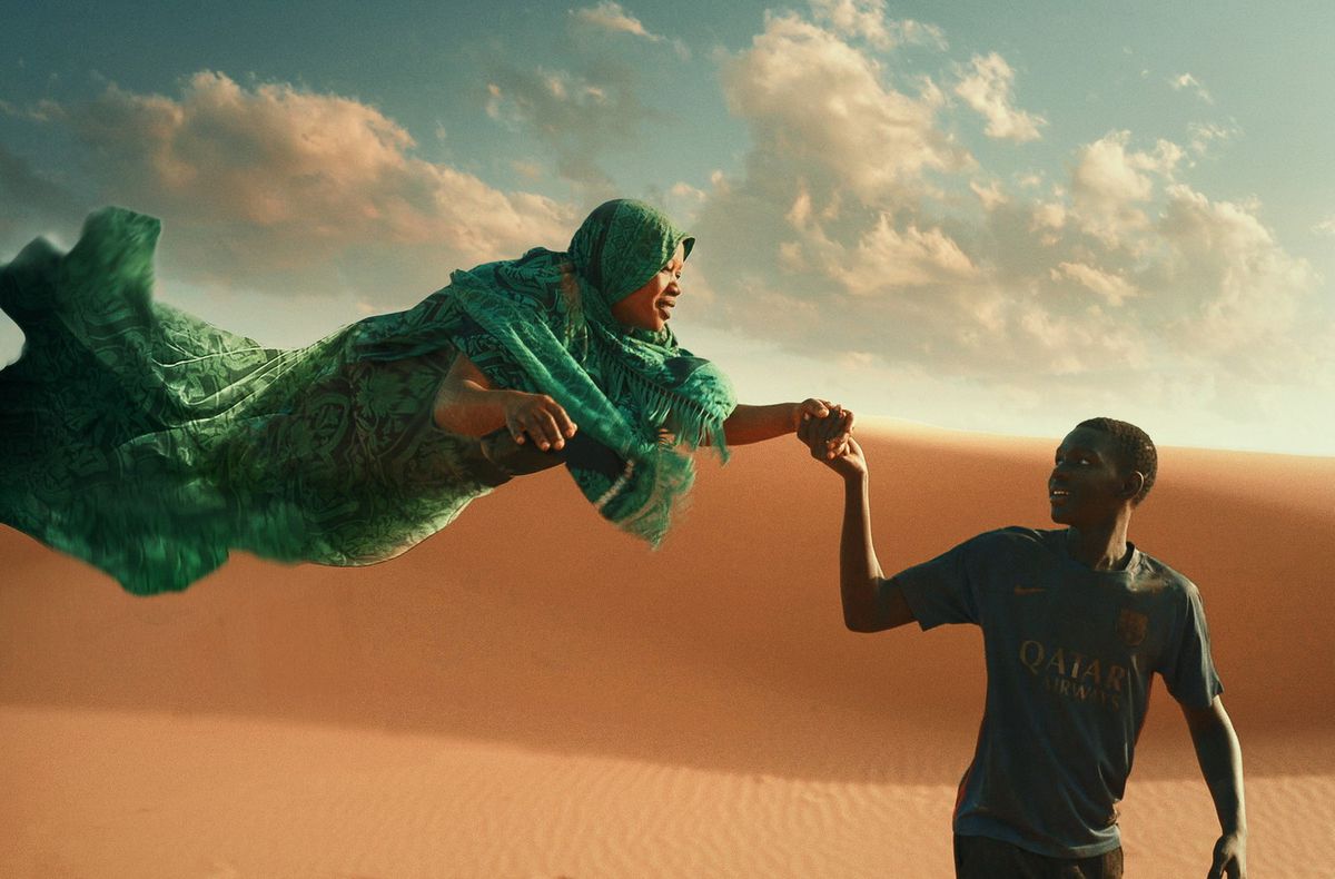 Хлопчик у футбольній формі тримає за руку жінку, одягнену в смарагдовий саван, що пливе пустелею.