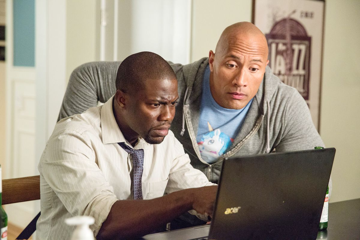 Dwayne Johnson mischievously peers over the shoulder at a laptop Kevin Hart is working on in the film Central Intelligence