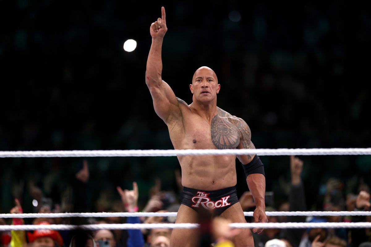 The Rock stands in the ring in branded trunks and a finger raised in the air at WrestleMania 40