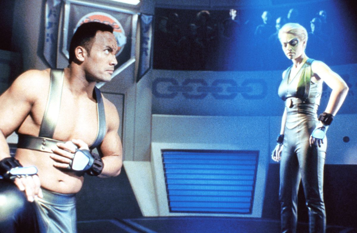 The Rock, in a funny sci-fi harness and alien makeup, stands in a ring opposite Seven of Nine in Star Trek: Voyager