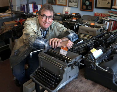A man sits among several typewriters in his Boston-area shop, which is currently for sale.